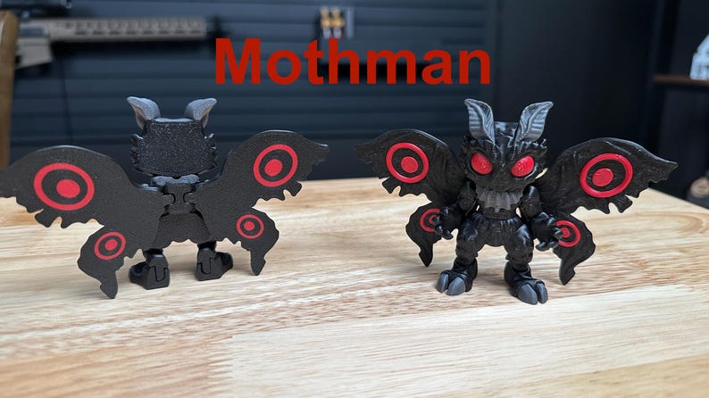 Puede incluir: Dos figuras de Mothman con cuerpos negros, alas texturizadas, patrones circulares rojos en las alas y ojos rojos brillantes. La palabra Mothman est&aacute; impresa en rojo sobre ellas. Las figuras tienen orejas puntiagudas y pies con garras, mostradas de frente y de espaldas.