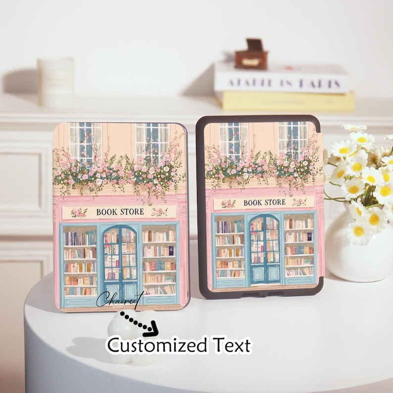 Op de afbeelding: Twee tablethoezen met een boekwinkelontwerp. De hoezen hebben een roze en blauwe gevel met de woorden "BOOK STORE" boven de ingang. Het ontwerp omvat ramen met bloemstukken en planken vol boeken. De onderkant van de hoes heeft de tekst "Customized Text".