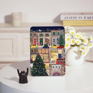 May include: A colorful illustration of a snowy city street at night with a large Christmas tree in the center. The street is lined with buildings decorated with lights and garlands. There are people walking and cars driving on the street. The illustration is set against a dark blue background with a crescent moon and stars.