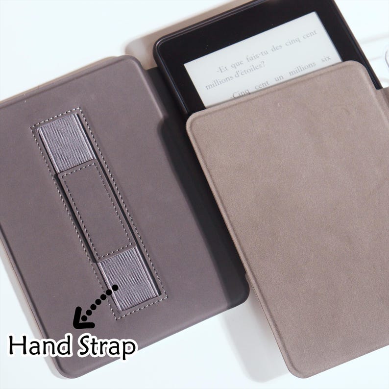 Op de afbeelding: Een grijze e-reader hoes met een handriem is open en toont het scherm van het apparaat. Het scherm toont tekst in een vreemde taal. De hoes is gemaakt van een zacht, getextureerd materiaal.