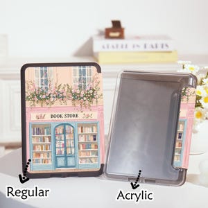 Op de afbeelding: Een reguliere en acryl e-reader case met een boekwinkelontwerp. Het ontwerp toont een roze gebouw met een blauwe deur, ramen en bloembakken. De tekst "BOOK STORE" staat boven de deur.