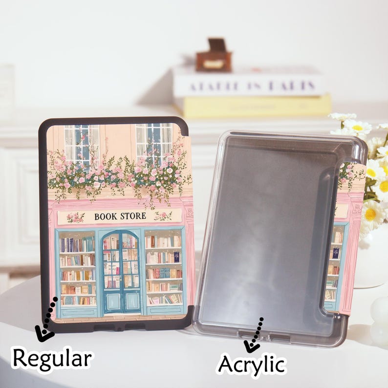 Op de afbeelding: Een reguliere en acryl e-reader case met een boekwinkelontwerp. Het ontwerp toont een roze gebouw met een blauwe deur, ramen en bloembakken. De tekst "BOOK STORE" staat boven de deur.