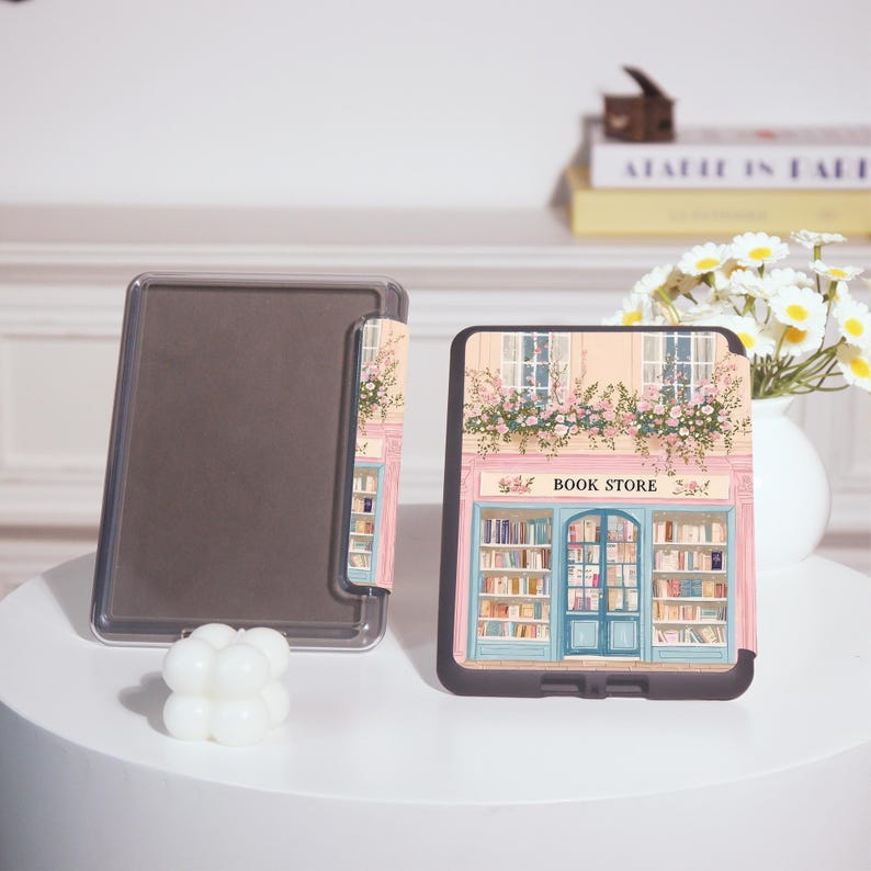 Op de afbeelding: Een zwarte tablet hoes met een kleurrijke illustratie van een boekhandelfa&ccedil;ade met de tekst "BOOK STORE". Het ontwerp omvat een blauwe deur, boekenplanken en bloemaccenten. Een doorzichtige tablethoes is ook zichtbaar.