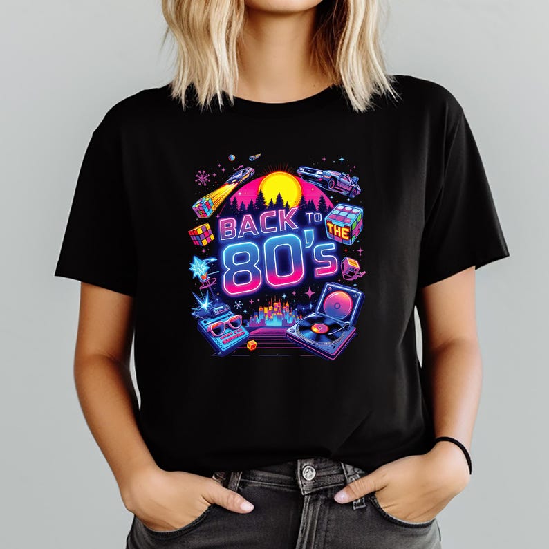 Puede incluir: Camiseta negra con un dise&ntilde;o gr&aacute;fico vibrante. El dise&ntilde;o presenta el texto "Back to the 80's" en colores ne&oacute;n, junto con elementos retro como un cubo de Rubik, un reproductor de casetes, un coche y un tocadiscos.