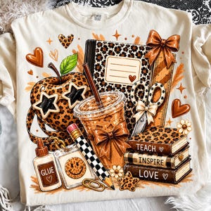 Puede incluir: Una camiseta color crema con un estampado gráfico de material escolar que incluye una manzana con estampado de leopardo y gafas de estrella, un cuaderno, tijeras, un lápiz, un bote de pegamento con la etiqueta GLUE y libros con TEACH, INSPIRE, LOVE.