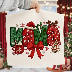 Puede incluir: Un letrero decorativo blanco con temática navideña con la palabra "MAMA" en verde y rojo. Las letras están decoradas con un gorro de Papá Noel, copos de nieve, un lazo y un árbol de Navidad. También aparece una taza de chocolate caliente.