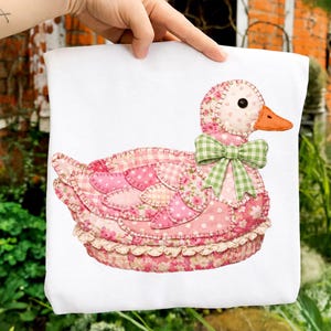 Puede incluir: Una funda de almohada blanca con un diseño de pato de patchwork. El pato tiene plumas rosas y con estampado floral, un lazo verde a cuadros y un pico naranja. El diseño tiene una estética encantadora y artesanal.