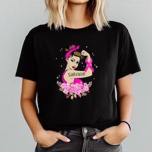 May include: Black t-shirt with a graphic of a woman flexing her arm with a pink ribbon, the word "SURVIVOR", and pink flowers. The woman wears a pink headband and top. The design is a symbol of breast cancer awareness.