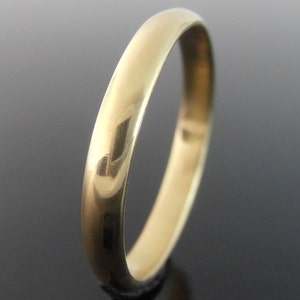 May include: A gold ring with a polished, reflective surface. The ring is a simple band design, catching the light and creating highlights. The ring's classic style makes it suitable for various occasions.