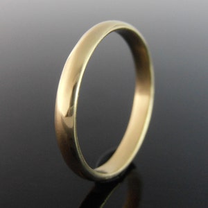 May include: A gold ring with a smooth, rounded band. The ring reflects light, creating highlights and shadows. The ring is a simple, classic design, suitable for everyday wear.