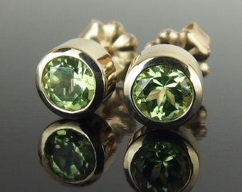 May include: A pair of gold earrings with green gemstones. The earrings are round and have a simple design.