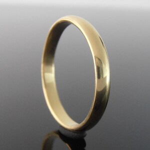 May include: A gold ring with a polished, rounded band. The ring's surface reflects light, showing highlights and shadows. The design is simple and classic, suitable for everyday wear or special occasions.