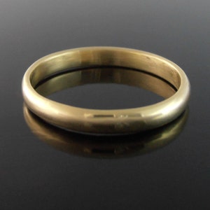 May include: A gold-coloured ring with a smooth, rounded design. The ring is made of a shiny, metallic material and reflects the light. The ring is a simple band, suitable for everyday wear.
