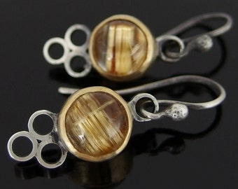 May include: A pair of silver earrings with gold accents. Each earring features a round, clear stone with gold flecks and a three-loop design.