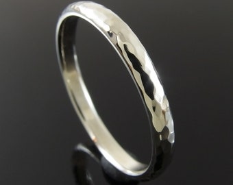May include: A silver ring with a hammered texture. The ring has a smooth, polished interior and a textured exterior. The ring is shown against a dark background.