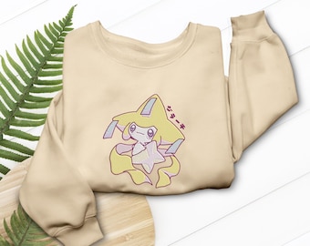 Puede incluir: Sudadera beige con un personaje de dibujos animados con detalles en amarillo, rosa y azul. El personaje tiene una cabeza en forma de estrella y pelo suelto. Texto japonés encima del personaje.