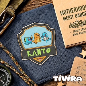 May include: A shield-shaped embroidered patch featuring cartoon characters Bulbasaur, Charmander, and Squirtle above the green text KANTO. The patch has a black border, a light blue background, and a small red and white circular icon at the bottom.