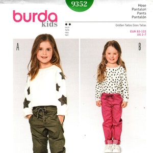 May include: Burda Kids sewing pattern number 9352 for pants with seam and hem allowances. The pattern includes two styles of pants, one with a star print and the other with a solid color. The pattern is for sizes EUR 92-122 (US 2-7).