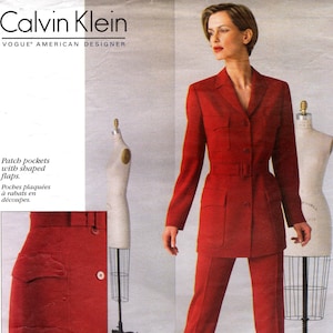 May include: A red Calvin Klein Vogue pattern featuring a woman in a red suit with a belted jacket and matching pants. The pattern includes patch pockets with shaped flaps. The Vogue logo and Calvin Klein branding are visible.