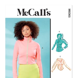 May include: McCall's sewing pattern M8365. The image shows a woman wearing a pink zip-up jacket and yellow leggings. The pattern includes illustrations of a hooded jacket and a collared top. The text "Designed and printed in USA" is also visible.
