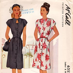 Puede incluir: Un patrón impreso McCall 6352 para un vestido, talla 14, busto 32. La ilustración muestra dos variaciones de un vestido de manga corta con botones frontales y cintura ceñida. Una versión es azul oscuro sólido y la otra es blanca con estampado floral rojo.