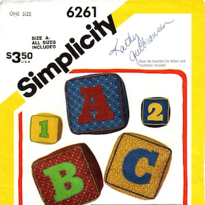 Könnte beinhalten: Ein Simplicity-Nähmuster zum Nähen eines Alphabetsatzes. Das Muster enthält Anleitungen zum Nähen von Blöcken mit den Buchstaben A, B, C und den Zahlen 1, 2 und 3. Das Muster enthält auch ein Bild von zwei Kindern, die mit den Blöcken spielen. Das Muster heißt "Simplicity 6261" und kostet 3,50 €.