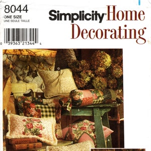 Puede incluir: Un patrón de costura Simplicity Home Decorating para almohadas. El patrón incluye instrucciones para hacer una variedad de almohadas, incluyendo una almohada de apoyo, una almohada cuadrada y una almohada rectangular. Las almohadas están decoradas con telas florales y a cuadros.