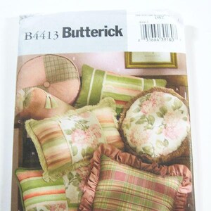 May include: Butterick B4413 pattern featuring various decorative pillows. The pillows showcase a mix of patterns, including stripes, floral prints, and plaid designs. Colors include shades of green, pink, and cream. The pattern includes a round pillow, a bolster, and square pillows.