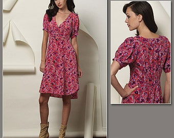 May include: A woman is wearing a pink and purple floral print dress with short sleeves and a V-neck. The dress has a fitted bodice and a flowing skirt.