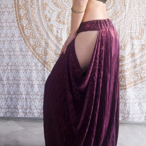 May include: A woman in a black and gold sequined crop top and a long, pleated, deep purple skirt with a thigh-high split. A gold and white mandala tapestry is in the background.
