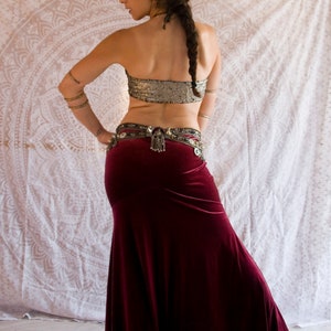 May include: A woman wearing a burgundy velvet skirt with a silver belt and a sequined silver top. She is wearing a gold headpiece and has her hair in a braid.