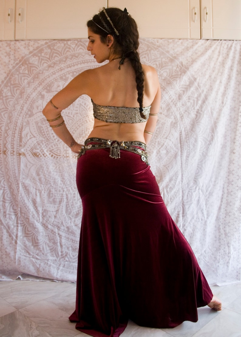 May include: A woman wearing a burgundy velvet skirt with a silver belt and a sequined silver top. She is wearing a gold headpiece and has her hair in a braid.