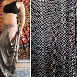 Könnte beinhalten: Ein schwarzes One-Shoulder-Crop-Top und eine graue, drapierte Hose. Die Hose hat einen hohen Schlitz an einer Seite. Der Stoff hat einen metallischen Glanz. Der Hintergrund zeigt einen farbenfrohen Wandteppich.