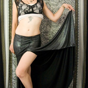 May include: A woman wearing a black lace top and a black skirt with a silver sheen. She is standing in front of a patterned background.