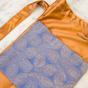May include: A gold drawstring bag with a blue and gold patterned lining. The bag has a long strap and a white toggle.
