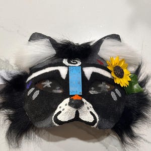 May include: Black and white furry mask with a painted face, a sunflower, and the text "冬眠" on the forehead.