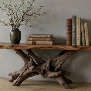 May include: A rustic wooden console table with a live edge top and a driftwood-style base. The table displays a dark vase with white flowering branches, and several books with titles like "Wabi Sabi Aesthetics" and "Japanese Garden Design".