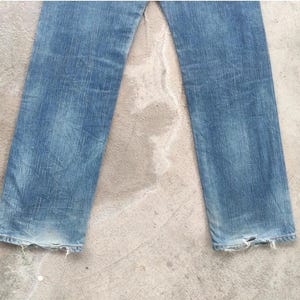 Puede incluir: Vaqueros de mezclilla azul claro con un lavado descolorido y detalles desgastados. Los vaqueros tienen un dise&ntilde;o cl&aacute;sico de cinco bolsillos y un corte de pierna recta. Los dobladillos est&aacute;n deshilachados.