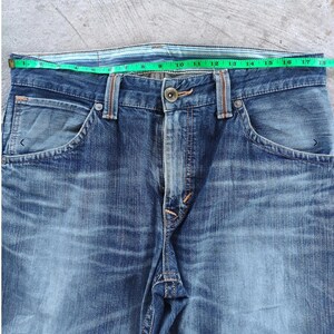 Peut inclure: Gros plan sur un jean en denim bleu avec une fermeture boutonn&eacute;e et des poches. La taille mesure environ 40,6 cm de large. Le jean a un d&eacute;lavage et est fait de denim durable.
