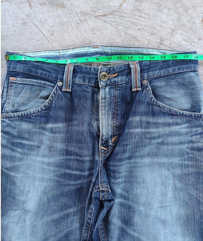 Peut inclure: Gros plan sur un jean en denim bleu avec une fermeture boutonn&eacute;e et des poches. La taille mesure environ 40,6 cm de large. Le jean a un d&eacute;lavage et est fait de denim durable.