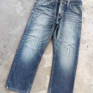 Peut inclure: Jean bleu d&eacute;lav&eacute; avec une conception classique &agrave; cinq poches. Le jean a une coupe droite et montre des signes d'usure, avec des zones plus claires sur les cuisses et les genoux. Le jean est pos&eacute; &agrave; plat sur une surface en b&eacute;ton.
