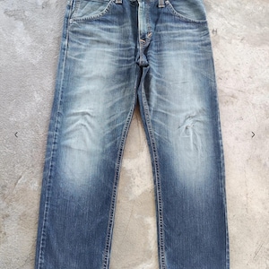 Peut inclure: Jean en denim bleu d&eacute;lav&eacute; avec une conception classique &agrave; cinq poches. Le jean a une coupe droite et pr&eacute;sente des signes d'usure, avec une d&eacute;coloration subtile et une zone us&eacute;e sur la jambe droite. La ceinture comporte des passants de ceinture et une fermeture boutonn&eacute;e.