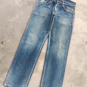Puede incluir: Vaqueros de mezclilla azul descolorido con un dise&ntilde;o cl&aacute;sico de cinco bolsillos. Los vaqueros tienen bragueta con botones y muestran signos de desgaste, con &aacute;reas m&aacute;s claras y una sutil decoloraci&oacute;n en toda la tela. Corte recto.