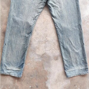 May include: Faded light blue denim jeans. The jeans have a classic five-pocket design and a straight leg cut. The denim appears worn and distressed, with subtle fading and creases. The jeans are laid flat, showcasing the front and upper portion of the garment.
