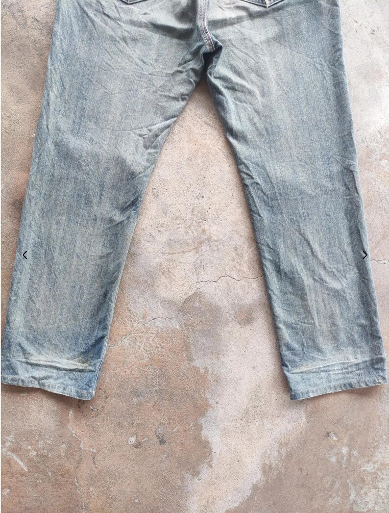 May include: Faded light blue denim jeans. The jeans have a classic five-pocket design and a straight leg cut. The denim appears worn and distressed, with subtle fading and creases. The jeans are laid flat, showcasing the front and upper portion of the garment.