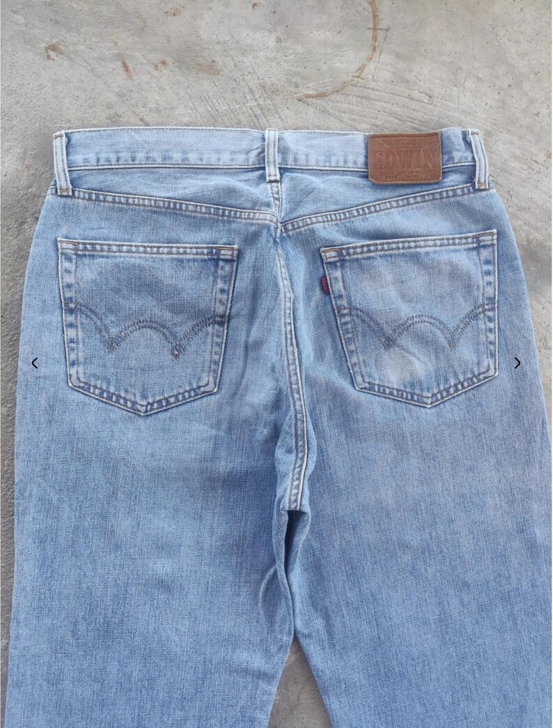 May include: Light blue denim jeans with classic five-pocket styling. Features a brown leather patch with embossed text and the iconic Levi's back pocket stitching. The jeans have a faded wash and a red tab on the back pocket.
