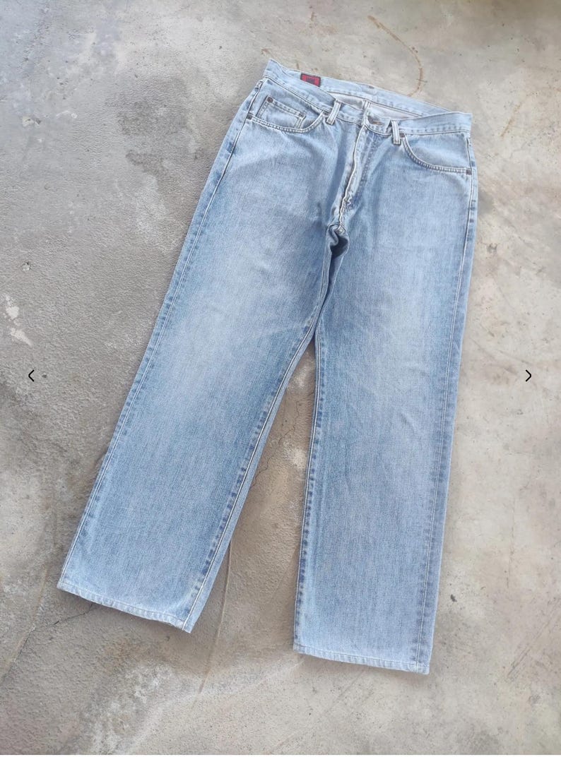 May include: Light blue denim jeans with a classic five-pocket design. The jeans have a straight leg cut and a button and zipper closure. The fabric appears to be a medium weight denim.