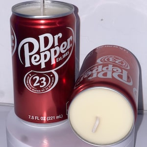 May include: Two red and white Dr Pepper-branded candles in the shape of a can. The candles are 7.5 fluid ounces (221 milliliters) each. The text on the cans reads "Dr Pepper Est. 1885" and "Authentic Blend of 23 Flavors".