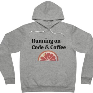 Puede incluir: Una sudadera con capucha gris con un cordón blanco y el texto "Running on Code & Coffee" con un gráfico de pomelo estilizado.