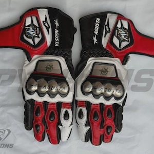 May include: Pair of black, white, and red motorcycle gloves. The gloves feature the "MV AGUSTA" logo and silver knuckle protectors. The design includes red accents on the fingers and wrist area, with white and black leather panels.
